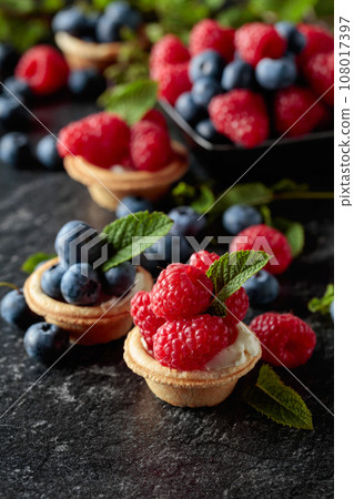 Small tartlets with fresh raspberries and blueberries on a black background. Small tartlets with fresh raspberries and blueberries on a black background. 108017397