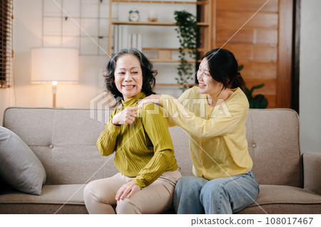 Happy adult granddaughter and senior grandmother having fun enjoying talk sit on sofa in modern living room, using a laptop, tablet bonding chatting relaxing at home together. Happy adult granddaughter and senior grandmother having fun enjoying talk sit on sofa in modern living room, using a laptop, tablet bonding chatting relaxing at home together. 108017467