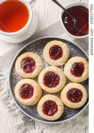 Thumbprint cookies are classic sugar cookies with a jam-filled center closeup on the plate on the white wooden table. Vertical top view 108017560