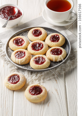 Thumbprint Christmas cookies filled with raspberry jam closeup on the plate served with tea on the wooden table. Vertical 108017566