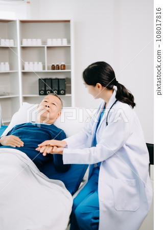 Asian doctor in white suit take notes while discussing and Asian elderly, man patient who lying on bed with receiving saline solution in hospital . Asian doctor in white suit take notes while discussing and Asian elderly, man patient who lying on bed with receiving saline solution in hospital . 108017816