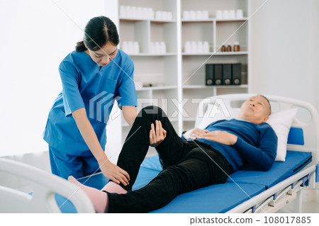 Physiotherapist Helping Patient While Stretching His Leg in bed in clinic . 108017885