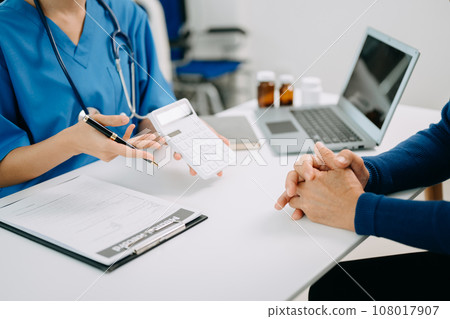 Healthcare costs and fees concept.Hand of smart doctor used a calculator and smartphone, tablet for medical costs at hospital in morning light. Healthcare costs and fees concept.Hand of smart doctor used a calculator and smartphone, tablet for medical costs at hospital in morning light. 108017907