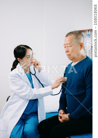 Asian doctor in white suit take notes while discussing and Asian elderly, man patient who lying on bed with receiving saline solution in hospital . Asian doctor in white suit take notes while discussing and Asian elderly, man patient who lying on bed with receiving saline solution in hospital . 108018068