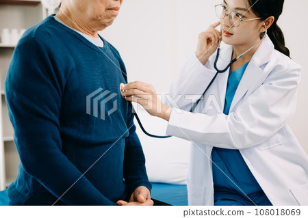 Asian doctor in white suit take notes while discussing and Asian elderly, man patient who lying on bed with receiving saline solution in hospital . Asian doctor in white suit take notes while discussing and Asian elderly, man patient who lying on bed with receiving saline solution in hospital . 108018069