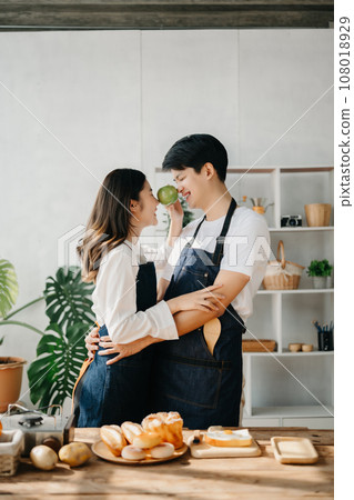 A man in the kitchen preparing a meal with Bread and fruit in cozy kitchen while his wife hugging him. sweet home. A man in the kitchen preparing a meal with Bread and fruit in cozy kitchen while his wife hugging him. sweet home. 108018929