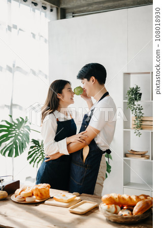 A man in the kitchen preparing a meal with Bread and fruit in cozy kitchen while his wife hugging him. sweet home. A man in the kitchen preparing a meal with Bread and fruit in cozy kitchen while his wife hugging him. sweet home. 108018930