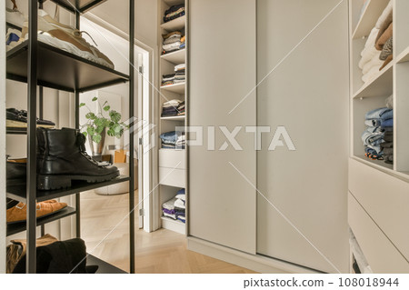 a walk - in closet with lots of clothes and shoes hanging on the wall behind it is an open white door a walk - in closet with lots of clothes and shoes hanging on the wall behind it is an open white door 108018944