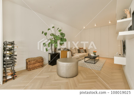 a living room with white walls and wood flooring, there is a large plant in the center of the room 108019025