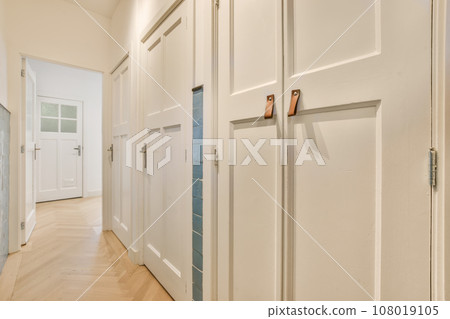 a long hallway with white walls and wood flooring the room is well lit by natural light from the windows a long hallway with white walls and wood flooring the room is well lit by natural light from the windows 108019105