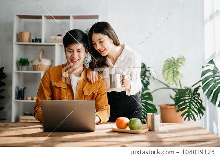 Two Asian business workers talking on the smartphone and using laptop at the home office. 108019123