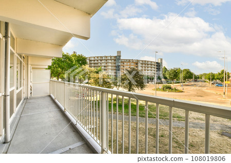 a balcony with white railings and trees in the foregrounded area on the other side of the building a balcony with white railings and trees in the foregrounded area on the other side of the building 108019806