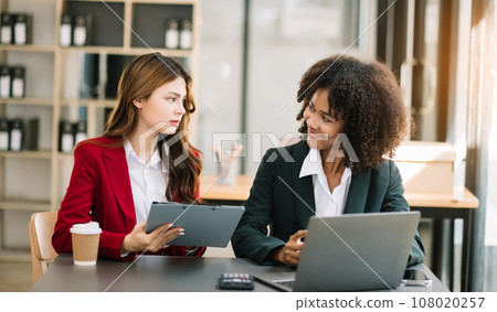 Businesswomen work and discuss their business plans. A Human employee explains and shows her colleague the results paper in modern office.. Businesswomen work and discuss their business plans. A Human employee explains and shows her colleague the results paper in modern office.. 108020257