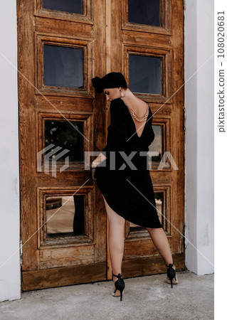 Stylish woman in the city. Fashion photo of a beautiful model in an elegant black dress posing against the backdrop of a building on a city street 108020681