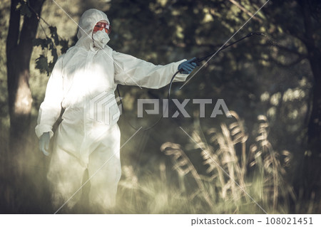 A worker sprays pesticides on trees outdoors. Tree pest control 108021451