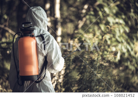 A worker sprays pesticides on trees outdoors. Tree pest control 108021452