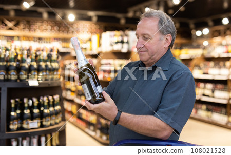 Mature man choosing fine bottle of champagne in supermarket 108021528