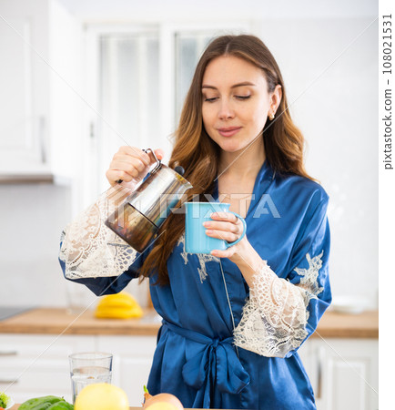 Woman dressed in a housecoat prepares coffee in the kitchen 108021531
