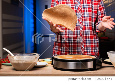 Woman cooking delicious crepe on electric pancake maker in kitchen, closeup 108021565