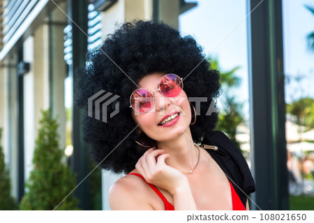 Girl with black curly hair in pink youth glasses, close-up portrait 108021650