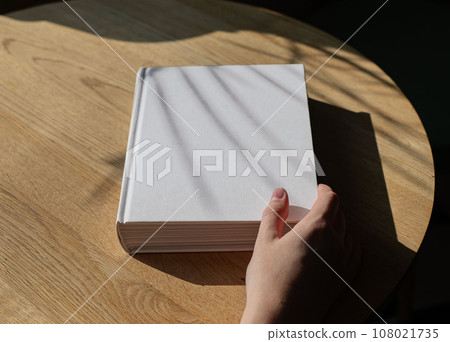 Book cover mockup on wood table. Hand holding literature mock up 108021735