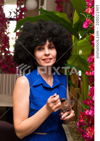 Middle aged woman with curly black hair eats ice cream 108021905