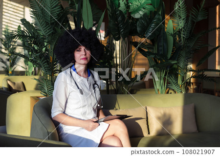 Nurse with black curly hair sits in hospital hallway, natural light Nurse with black curly hair sits in hospital hallway, natural light 108021907