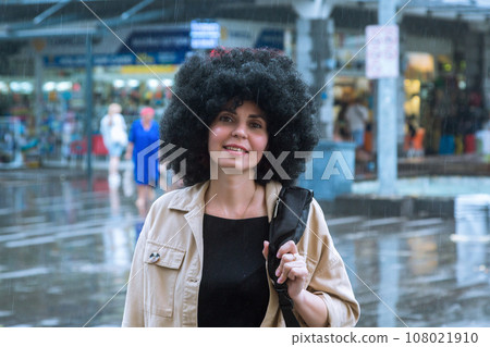 A girl with lush curly hair walks through the city in the rain 108021910