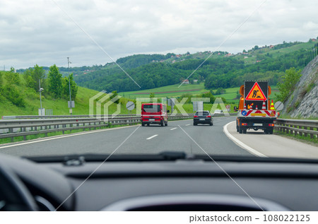 Driving on a highway passing by a road maintenance vehicle - view from a car windshield Driving on a highway passing by a road maintenance vehicle - view from a car windshield 108022125
