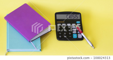 The word Crisis on a calculator, notepads lie next to it on a yellow background 108024313