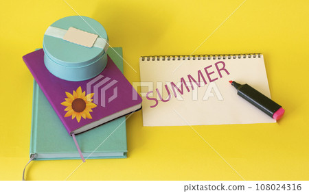 summer text written on a white sheet, near bright notebooks and a yellow background 108024316