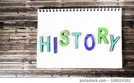 The word history is written in multicolored wooden letters on a white notebook. Wooden background. The word history is written in multicolored wooden letters on a white notebook. Wooden background. 108024382