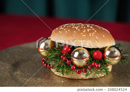 Creative Christmas hamburger. Burger made from fir branches and Christmas ornaments on holiday table. Creative New Year or Christmas food concept. 108024524