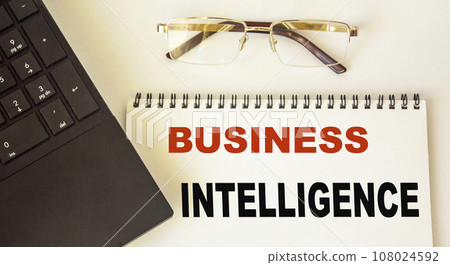 Business analytics text written on a notebook, next to a laptop and glasses on a white background 108024592