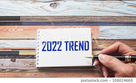 Female hand writes the text TREND 2022 on a notebook. Business concept Female hand writes the text TREND 2022 on a notebook. Business concept 108024668