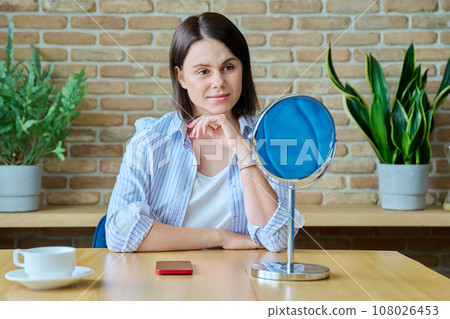 Young happy brunette looking at her face in mirror Young happy brunette looking at her face in mirror 108026453