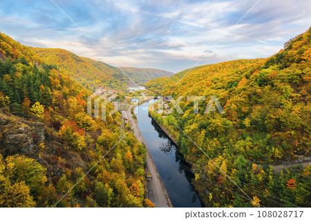 river flows through countryside valley view from above. mountainous landscape of romania in autumn. scenery with cloudy sky in evening light river flows through countryside valley view from above. mountainous landscape of romania in autumn. scenery with cloudy sky in evening light 108028717