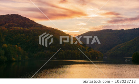 mountainous autumn landscape with lake at dusk. scenery in fall colors reflecting in the calm water. local tourism and relaxation concept. cluj county, romania 108028718