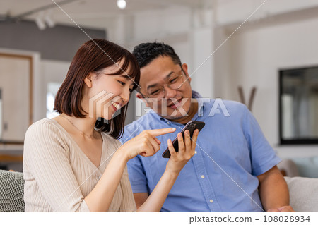 A man and a woman using smartphones in the living room A man and a woman using smartphones in the living room 108028934