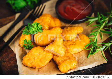 Semifinished Breaded chicken nuggets from chicken fillet on a dark background with fresh herbs. Quick cooking at home. Fast food. Breaded Chicken Inner Fillet. Fast cooking.Chicken nuggets with salad. 108029197