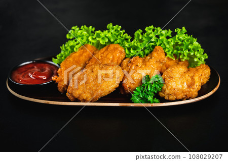 Chicken wings fried until half cooked, semi-finished product.Semi-finished chicken wings on a dark background with fresh herbs. Half-finished. Quick cooking at home.Fast food. Breaded chicken wings. 108029207