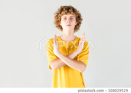 Protest and dissent is shown by handsome curly haired guy in yellow t-shirt crossing his arms Protest and dissent is shown by handsome curly haired guy in yellow t-shirt crossing his arms 108029529