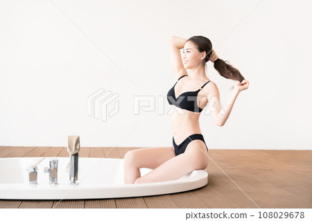 Beautiful Korean girl in black swimsuit sitting on round bubble bath in modern interior. 108029678