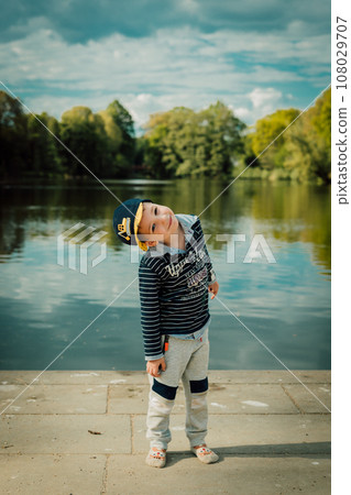 A small child stands near a lake in a park in the summer 108029707
