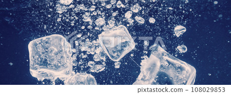 Water splashing and ice cube. Ice splashing into a glass of water. Underwater pouring ice cubes falling into clear watering background. Refreshing chill drinking. Ices in a glass with blue background 108029853