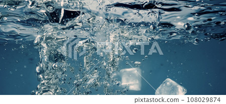 Water splashing and ice cube. Ice splashing into a glass of water. Underwater pouring ice cubes falling into clear watering background. Refreshing chill drinking. Ices in a glass with blue background 108029874