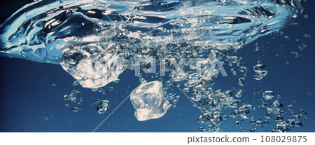 Water splashing and ice cube. Ice splashing into a glass of water. Underwater pouring ice cubes falling into clear watering background. Refreshing chill drinking. Ices in a glass with blue background 108029875