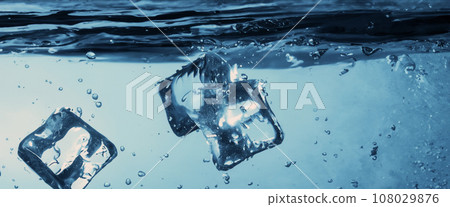 Water splashing and ice cube. Ice splashing into a glass of water. Underwater pouring ice cubes falling into clear watering background. Refreshing chill drinking. Ices in a glass with blue background 108029876