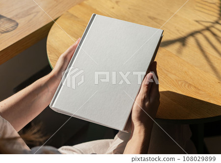 Book mock up, hand holding hard cover mockup on wood table 108029899