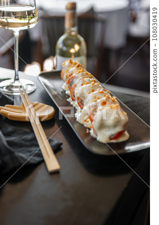 Sushi roll with salmon and vegetables in sauce on a black plate in a restaurant 108030419